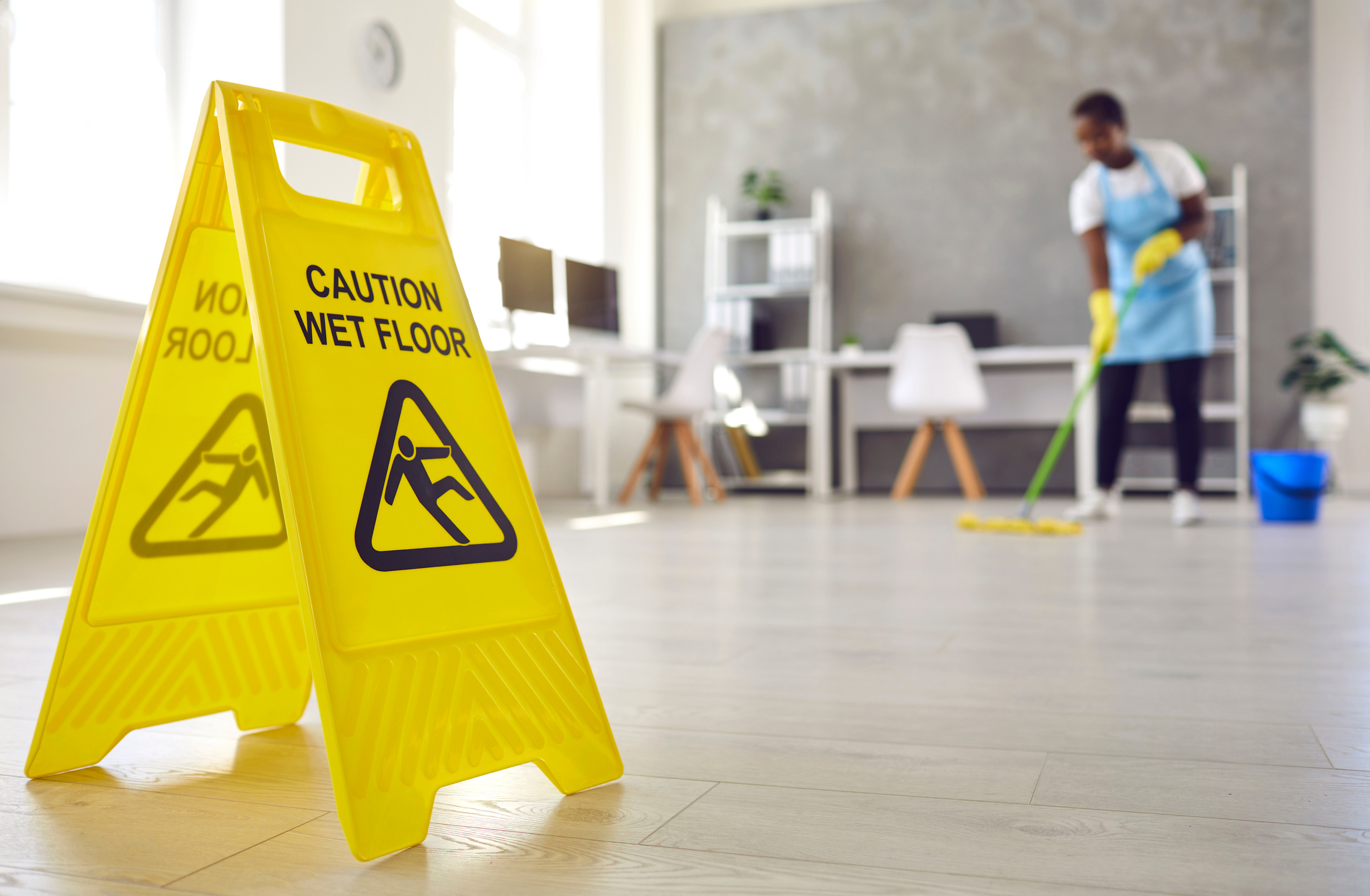 Close up of Sign Warning about Wet Floor Placed by Janitor Who's Working in Background